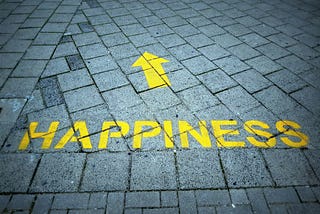 Word happiness on cobble stone path with arrow pointing ahead supporting Thomas McCorry article
