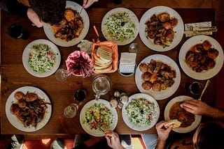 A table view from the top showing variety of food and just hands of people.