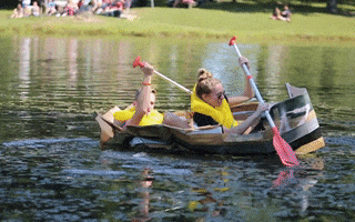 Two people in a cardboard boat that is barely floating paddling together