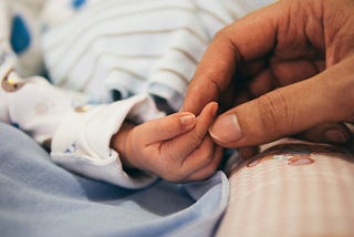 A parent holds the tiny hand of a newborn baby.