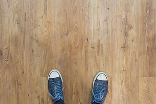 Two blue shoes on a light brown hard wood floor.