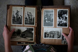 A person flipping through an old photo album filled with black-and-white snapshots of family memories, including horseback riding, holiday celebrations, and vintage cars.