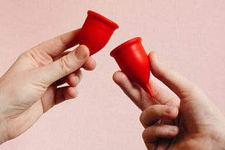 Two red menstrual cups held in two hands. Menstrual cup guide