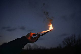 A hand holding a paper on fire against the night sky