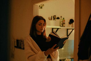 A girl wearing a white cardigan and enjoying her time reading a book