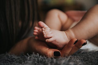 An adult hand cradeling the feet of a newborn baby.