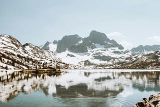 A snow-covered mountain peak mirrors itself on a lake which features a ripple effect in the water.