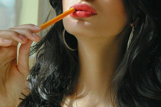 Close-up of a brunette wearing red lipstick chewing on a pencil.