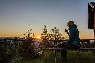 picture of a lady dressed in a jacket with a cup of cofee watching the sunrise
