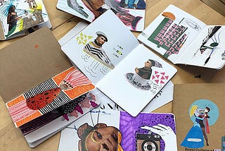 Many notebooks open on a table showing surreal doodles and cut up art