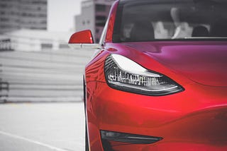 A red sporty car with high rise buildings in the background.