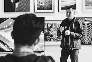 A person stands in front of a wall of art telling a story to a room full of people