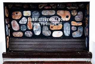 A mural behind a bench of different coloured and patterned shapes with text over that says “Our differences don’t have to divide us”.