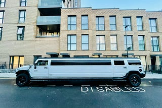 A chunky white party limousine parked on a disabled parking spot.