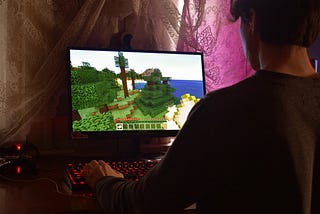 Why you should let your husband and kids play video games. A guy playing the videogame Minecraft on their desktop PC with their keyboard backlit with red.