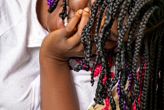 A young black girl with colorful braids with her head on her hand.