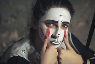 Person in mime make-up drawing red tears down their face