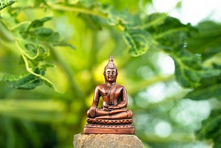 A miniature budist statute with green leaves on the background