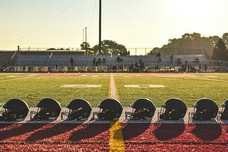 Seven football helmets lined up on the ground next to the 50 yard-line.