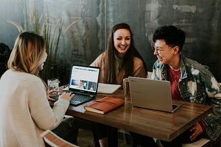 Designers smiling sitting around a table with their laptops.