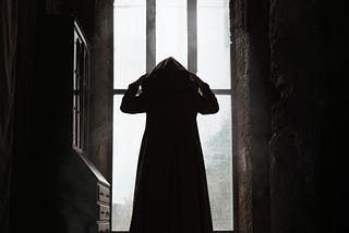 Cloaked silhouette in some sort of olde timey building like a castle or a church