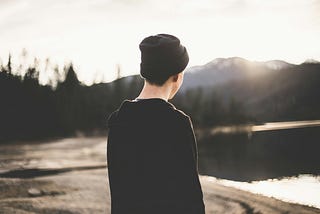 Boy with a black beanie looking out at sunrise by a lake