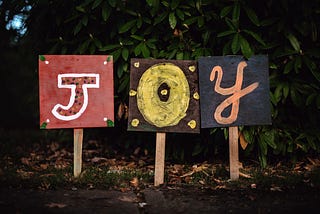 Three signs next to each other, spelling out the word “Joy”