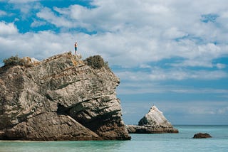 swimmer standing at top of cliff beside the ocean