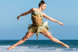 fit and free woman doing a ballet leap on the shoreline