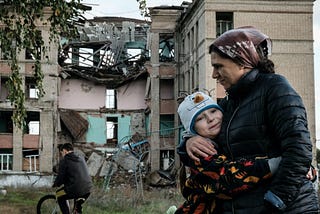 A woman hugging a child in front of a destroyed building