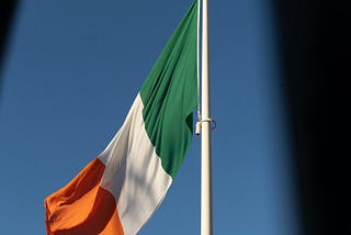 Irish flag (green at the hoist-white-orange in equal ratios) flying against a blue background