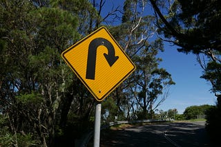 Yellow road sign with black curved arrow indicating turning around.