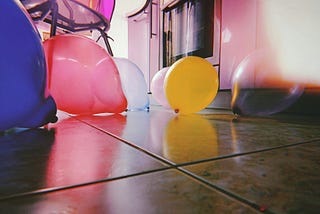 An array of balloons is spread out on a tile floor, a red, yellow, blue, and white one