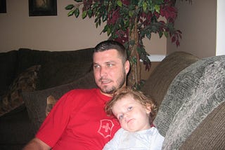 A man sitting on the sofa with his toddler daughter on his lap.