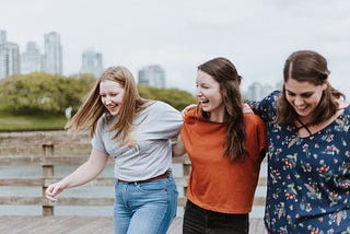 Three young women are walking arm in arm and laughing very joyfully.