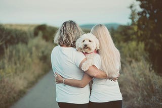 Man and a woman on a countryside path with the arms around one another while holding their dog