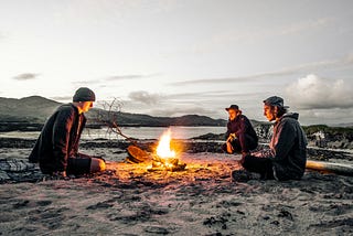 3 men sitting around a survival camp fire.