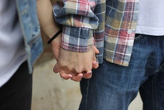 Two people wearing casual clothes hold hands. All you see in the photo is part of their bodies and their clasped hands.