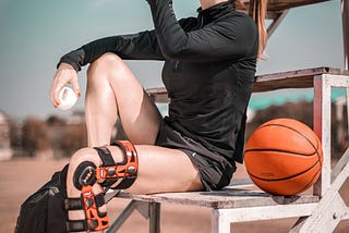 Sporty woman with a knee brace on sipping water while resting in between exercising.