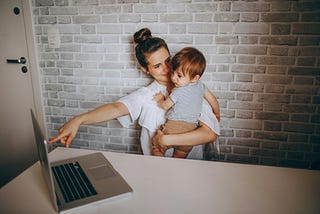 Woman holding child and pointing at a laptop.