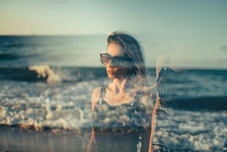 A woman stands by the sea, her silhouette blending with the waves in a double-exposure effect. The image captures both strength and vulnerability, reflecting the journey of overcoming life’s challenges with calm determination.