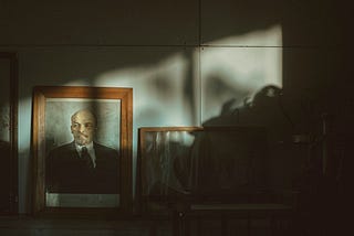 A darkened room lit by a little outside light showing a portrait of Vladmir Lenin