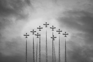 Jets surge skyward in a perfect arrow, smoke trails forming a sharp spearhead in the clouds, a monochrome symbol of teamwork, leadership, progress and upward momentum.