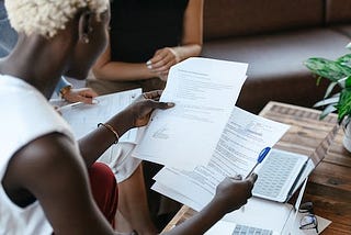 a black lady with blonde hair holding up documents with a laptop on her table.