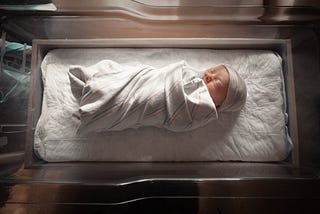 A newborn baby swaddled in a hospital infant bed