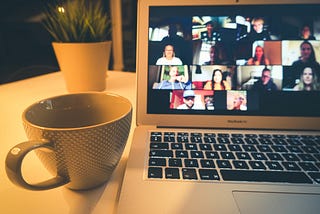 A desk with a plant, coffee cup and a Macbook showing a Zoom event on the screen.