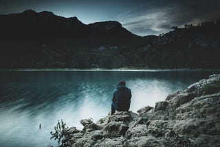 A person sits alone at a lake