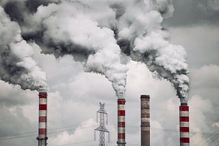 Image of red and white chimneys pumping smoke into the air from a power plant