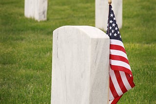 Mickey Markoff Air Sea Exec 2024 — Grey gravestone with American flag in green grass posted on mickey markoff article on the net worth of legacy and paying tribute to veterans