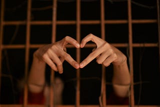 A person behind bars forming a heart with their fingers